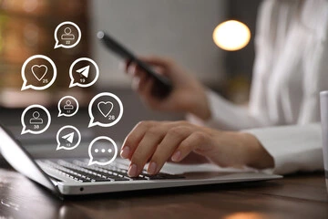 Person managing social media notifications on laptop and smartphone, representing real-time engagement and SMM in digital marketing.